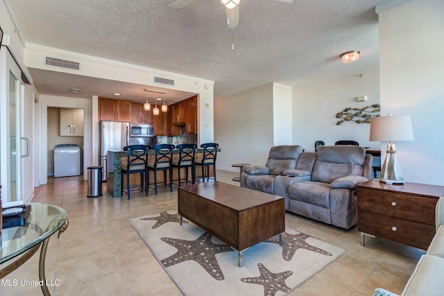 living area featuring a ceiling fan, visible vents, a textured ceiling, and washer / dryer