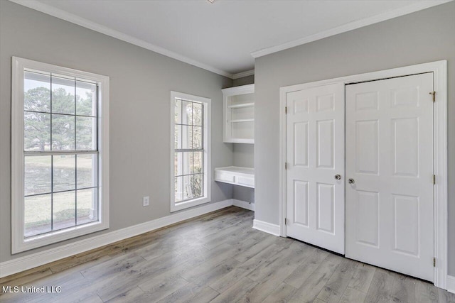 unfurnished bedroom featuring built in study area, crown molding, light wood-style flooring, and multiple windows