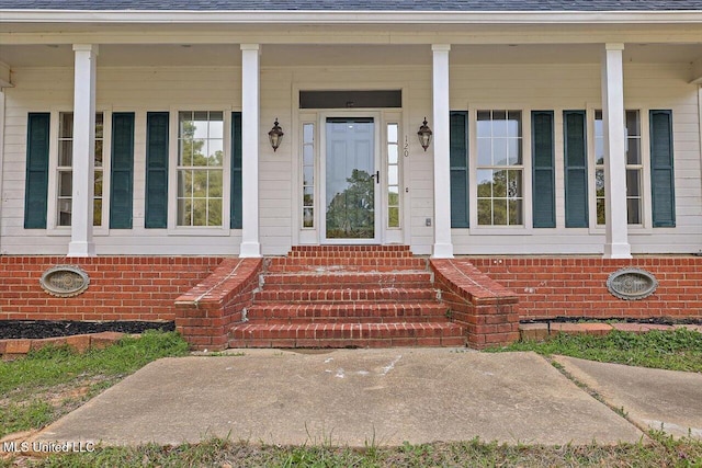 view of exterior entry with covered porch and roof with shingles