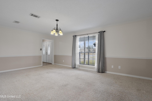 carpeted spare room featuring ornamental molding, a textured ceiling, and a chandelier