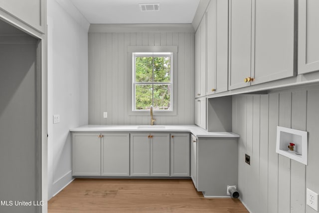 clothes washing area featuring cabinets, hookup for a washing machine, sink, and light wood-type flooring