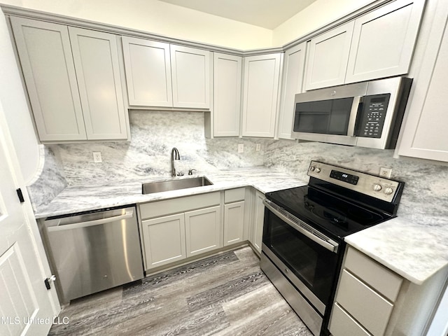 kitchen featuring gray cabinetry, backsplash, sink, hardwood / wood-style flooring, and stainless steel appliances