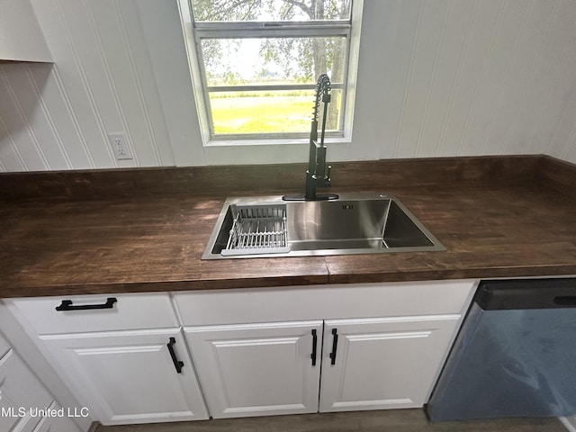 room details featuring stainless steel dishwasher, dark countertops, a sink, and white cabinets