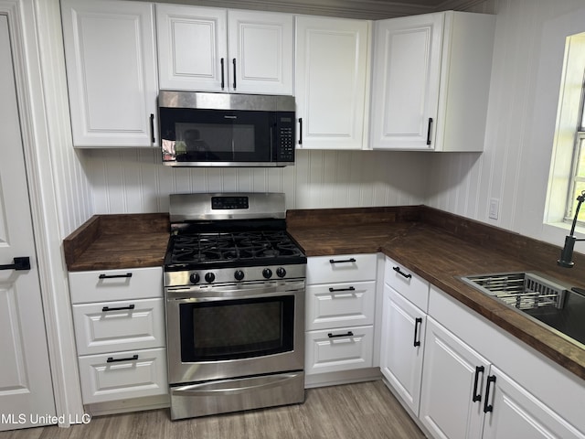 kitchen with appliances with stainless steel finishes, wooden counters, and white cabinetry