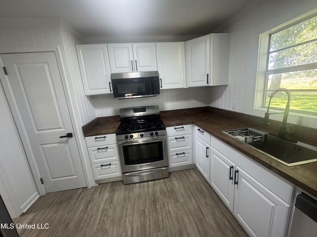kitchen with a sink, appliances with stainless steel finishes, wood finished floors, and white cabinets