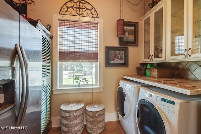 washroom with a wealth of natural light, dark tile patterned floors, washing machine and dryer, and cabinets