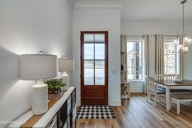 entryway featuring baseboards, ornamental molding, light wood-style flooring, and a notable chandelier