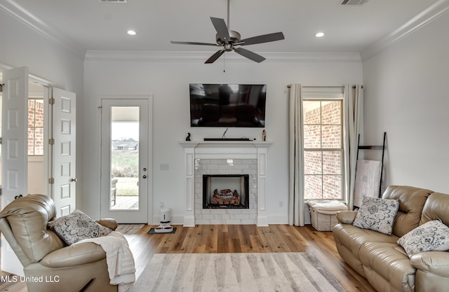 living room with light wood finished floors, a fireplace, crown molding, and recessed lighting