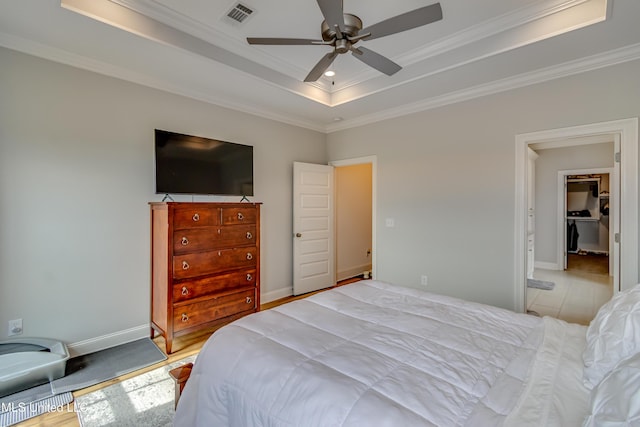 bedroom with a ceiling fan, visible vents, baseboards, a tray ceiling, and crown molding