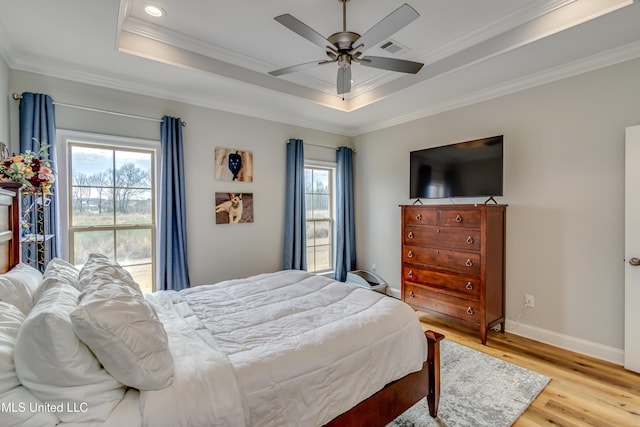 bedroom featuring light wood-style floors, baseboards, a tray ceiling, and crown molding