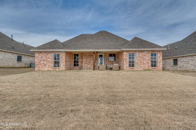 back of property with brick siding, a lawn, and roof with shingles