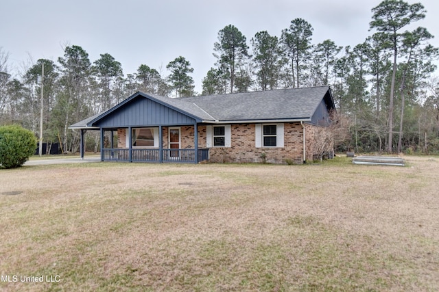 view of front of property featuring a front yard, brick siding, covered porch, and a shingled roof