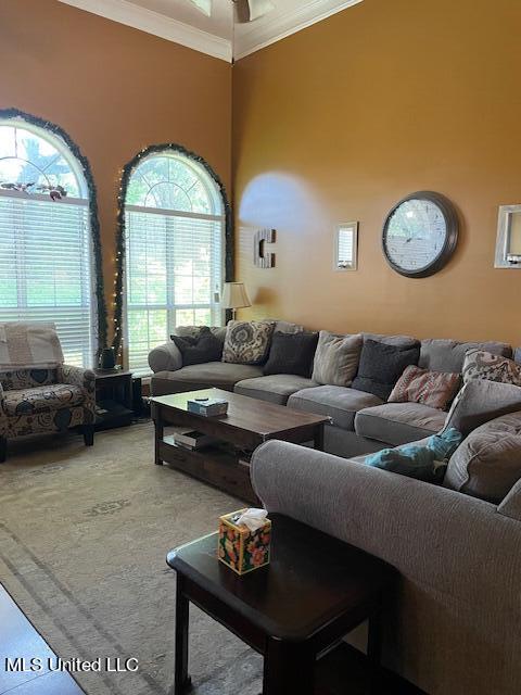 carpeted living room with crown molding, ceiling fan, and a towering ceiling