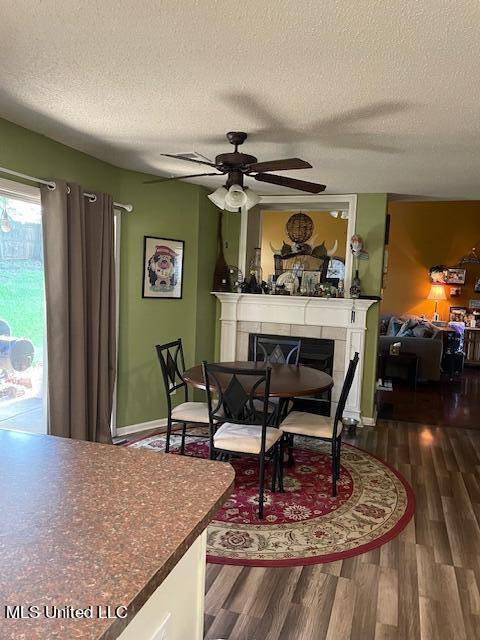 dining room featuring ceiling fan, a fireplace, dark hardwood / wood-style flooring, and a textured ceiling