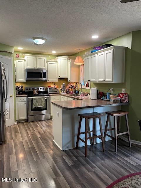 kitchen featuring white cabinetry, a kitchen breakfast bar, stainless steel appliances, decorative light fixtures, and kitchen peninsula