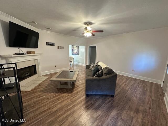 living room featuring dark hardwood / wood-style floors, ceiling fan, ornamental molding, and a tiled fireplace