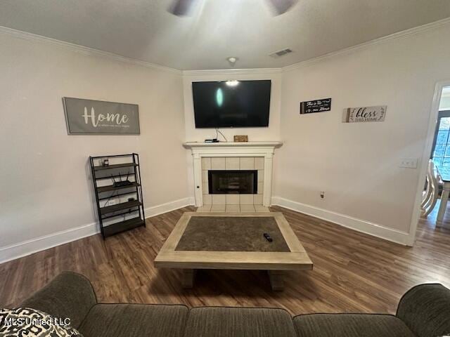 living room with ceiling fan, crown molding, dark wood-type flooring, and a tiled fireplace