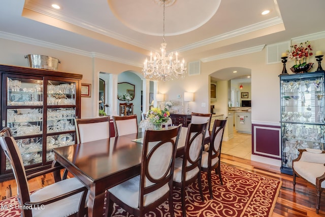 13129 Jordan Bluff Rd, Kiln, MS 39556 - dining room with arched walkways, a raised ceiling, light wood-type flooring, a chandelier, and ornamental molding
