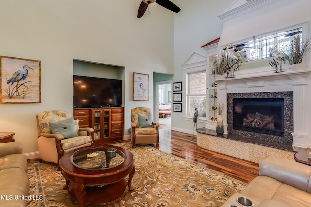 13129 Jordan Bluff Rd, Kiln, MS 39556 - living room featuring wood finished floors, baseboards, ceiling fan, a towering ceiling, and a premium fireplace