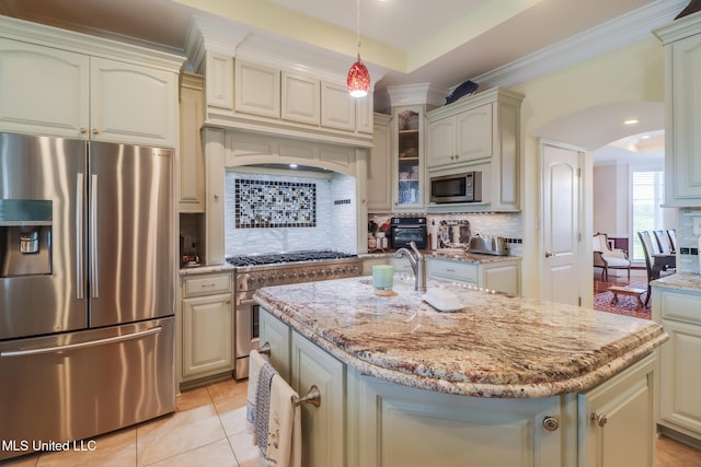 13129 Jordan Bluff Rd, Kiln, MS 39556 - kitchen with stainless steel appliances, arched walkways, light stone counters, decorative backsplash, and a kitchen island with sink