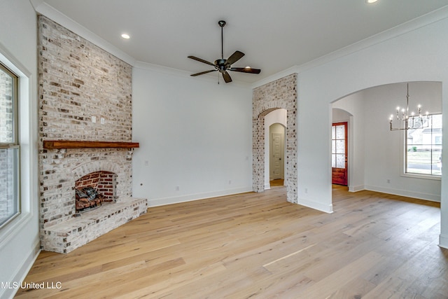 unfurnished living room featuring ceiling fan with notable chandelier, light wood-type flooring, crown molding, and a brick fireplace