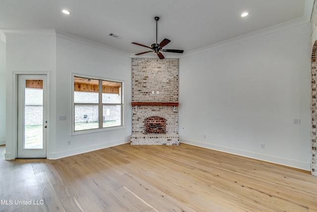 unfurnished living room with light wood-type flooring, a brick fireplace, ceiling fan, and crown molding