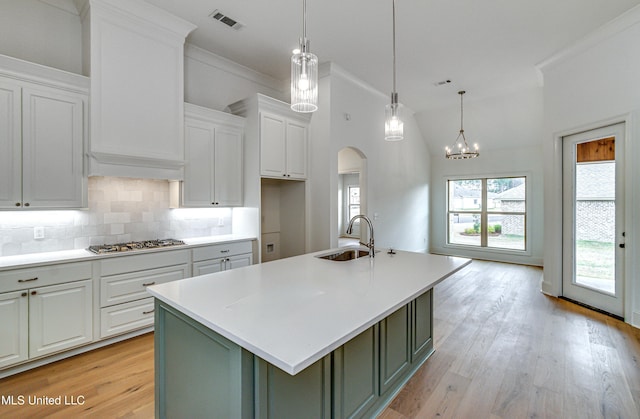 kitchen with sink, light hardwood / wood-style flooring, white cabinetry, hanging light fixtures, and an island with sink