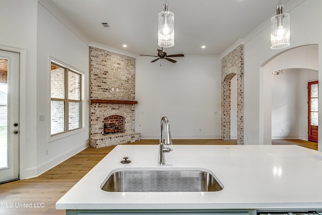 kitchen with sink, light hardwood / wood-style flooring, pendant lighting, a kitchen island with sink, and a fireplace