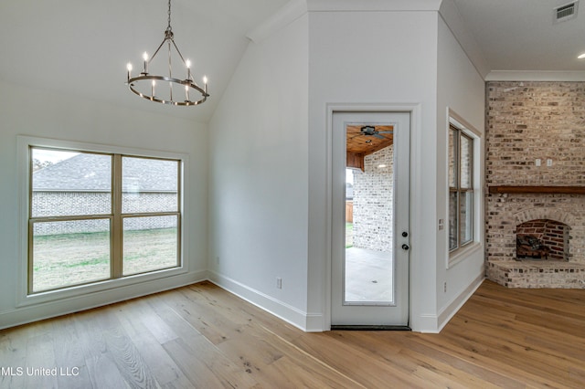 entryway with crown molding, vaulted ceiling, light hardwood / wood-style flooring, a fireplace, and a chandelier