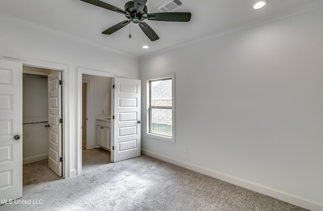 unfurnished bedroom featuring a closet, ensuite bath, ceiling fan, and light colored carpet