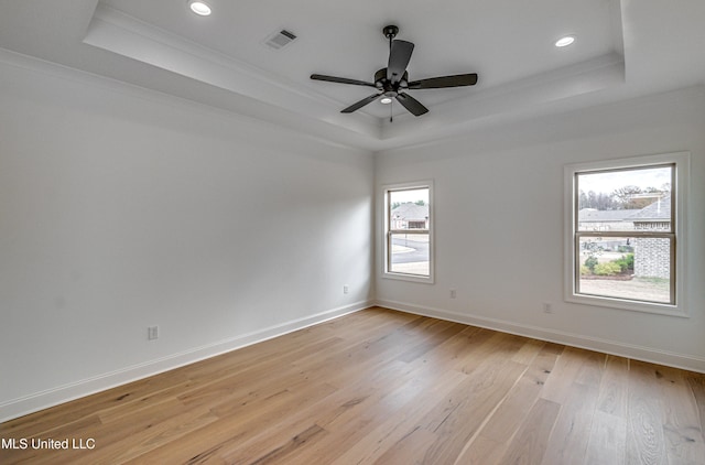 unfurnished room featuring ceiling fan, a raised ceiling, light wood-type flooring, and crown molding