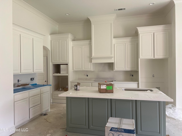 kitchen with stovetop, crown molding, white cabinetry, and an island with sink