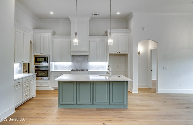 kitchen with stainless steel appliances, sink, decorative light fixtures, light hardwood / wood-style flooring, and an island with sink