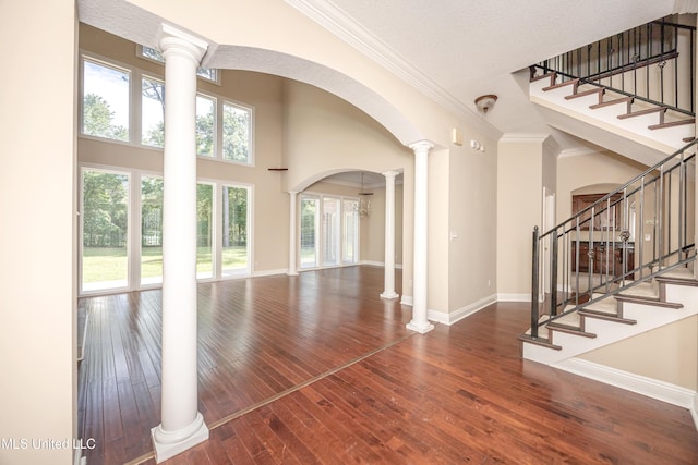 unfurnished living room featuring hardwood / wood-style floors, crown molding, baseboards, decorative columns, and a high ceiling