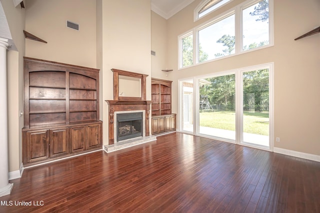 unfurnished living room featuring a high ceiling, a fireplace, wood-type flooring, baseboards, and crown molding