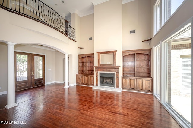 unfurnished living room with ornate columns, arched walkways, built in shelves, french doors, and a towering ceiling