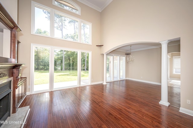 unfurnished living room featuring decorative columns, a high end fireplace, dark wood-type flooring, baseboards, and a towering ceiling