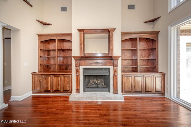 unfurnished living room featuring dark wood finished floors, a premium fireplace, a towering ceiling, and baseboards