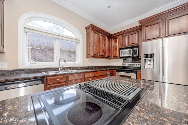 kitchen featuring appliances with stainless steel finishes, a sink, crown molding, dark stone countertops, and brown cabinets