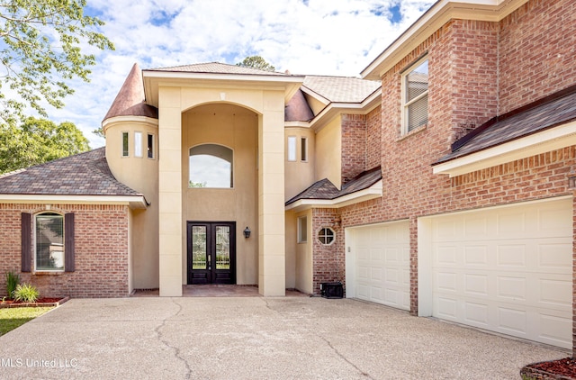 property entrance featuring french doors, concrete driveway, brick siding, a garage, and roof with shingles