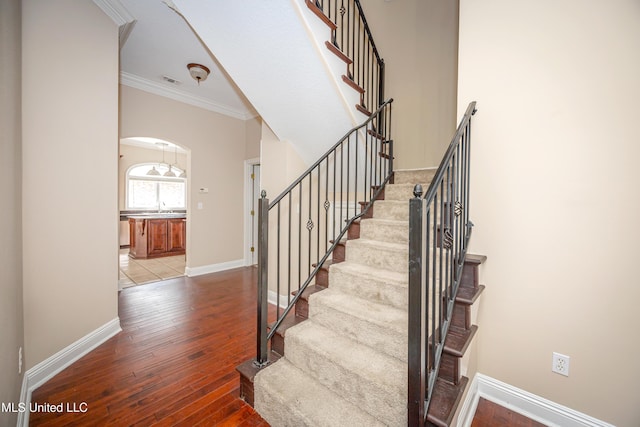 stairs featuring hardwood / wood-style floors, baseboards, crown molding, and arched walkways