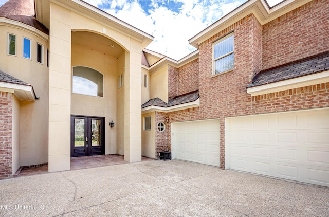 doorway to property with french doors, driveway, brick siding, a garage, and stucco siding