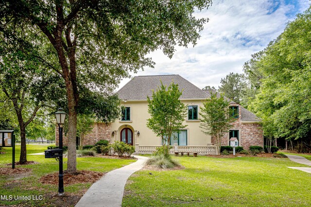 view of front facade with stucco siding, a front lawn, and roof with shingles