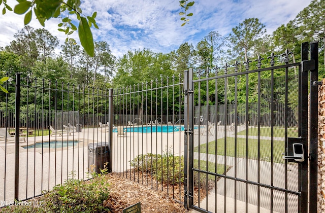 gate with fence, a community pool, view of wooded area, and a patio