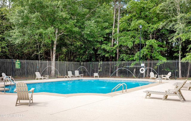 community pool with a patio area, fence, and view of scattered trees
