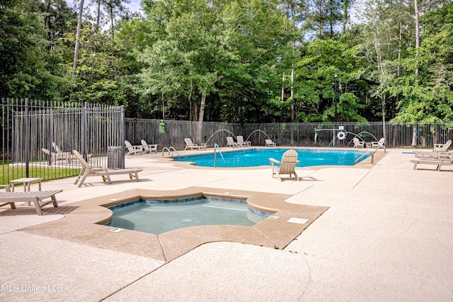community pool featuring fence, a patio, view of scattered trees, and a hot tub