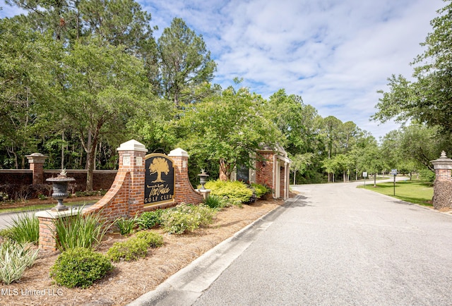 community sign featuring fence, view of wooded area, and a gate