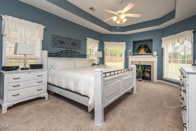 carpeted bedroom with ceiling fan, multiple windows, and a raised ceiling