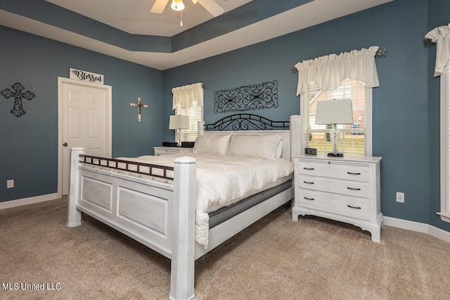 carpeted bedroom with a raised ceiling and ceiling fan