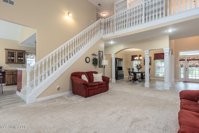 living room with a towering ceiling, an inviting chandelier, light carpet, and decorative columns